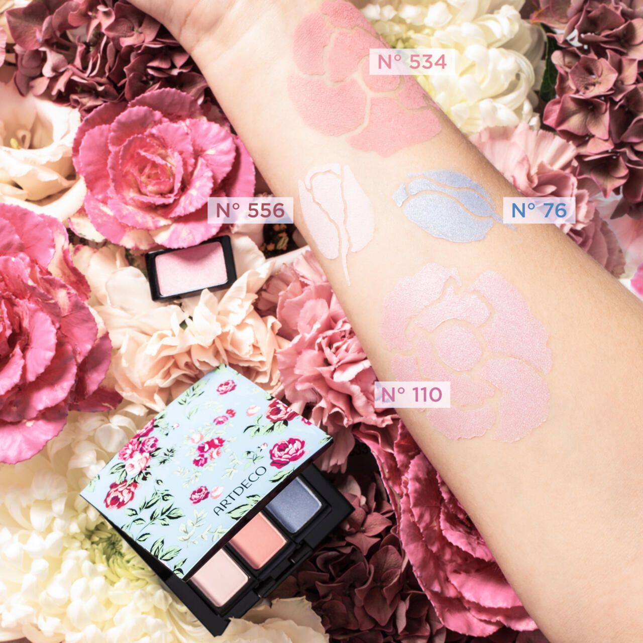 Artdeco Eyeshadow-Palette mit vier Farben. Auf einem Arm sind verschiedene Farbtöne aufgetragen. Blumen im Hintergrund.