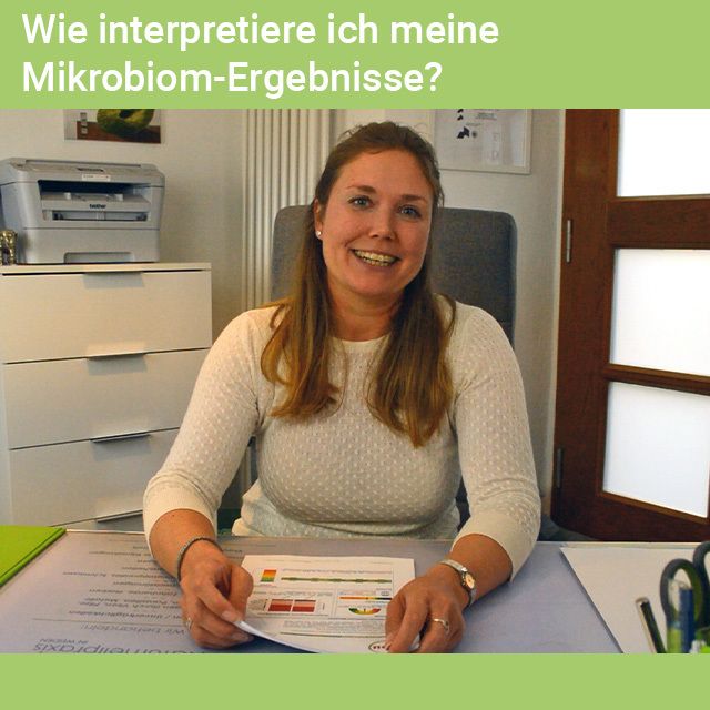 Frau sitzt an einem Schreibtisch, hält ein Blatt Papier. Auf dem Tisch: Drucker, Stifte. Hintergrund: Büro. Text: Wie interpretiere ich meine Mikrobiom-Ergebnisse?