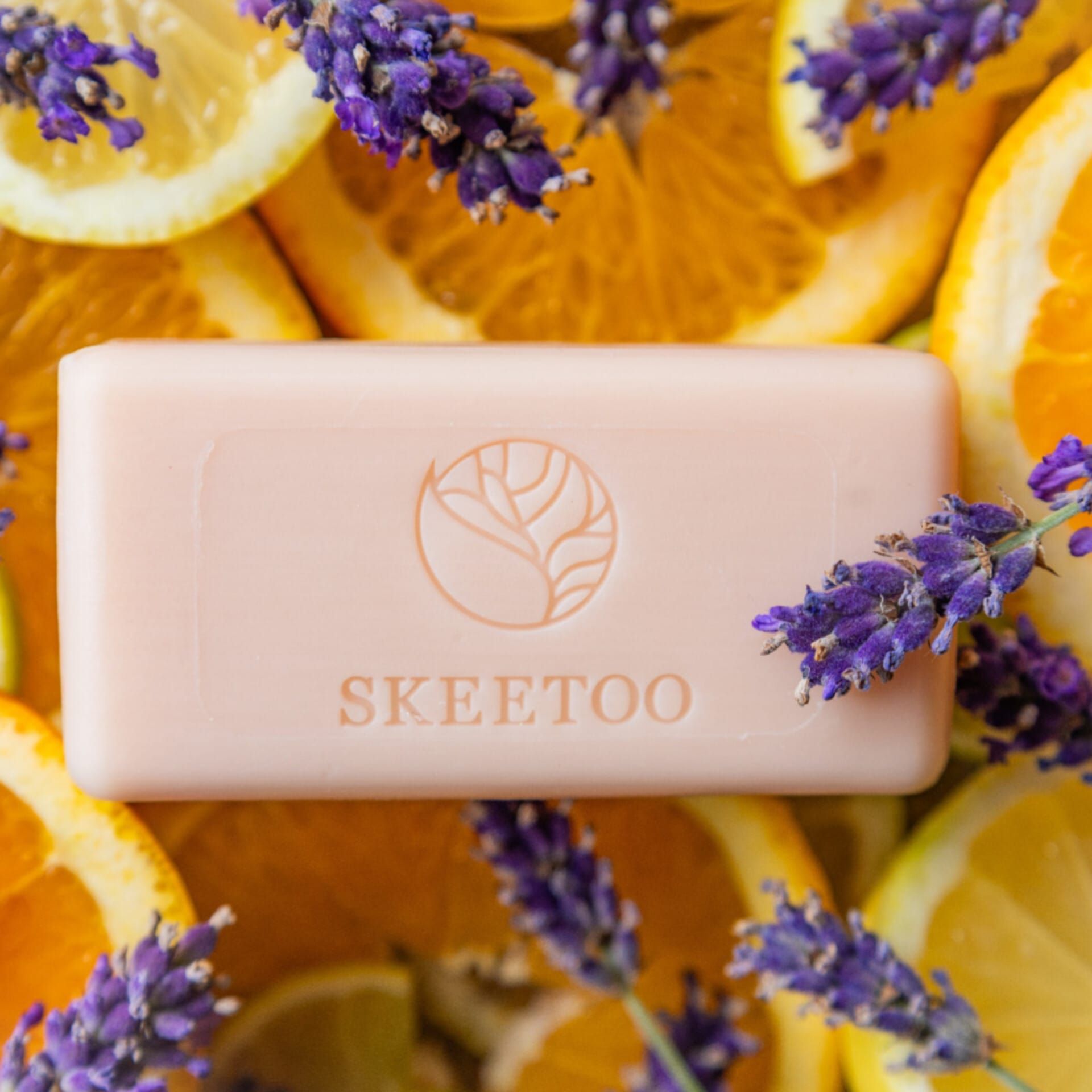 Rosa Seife mit SKEETOO-Logo, umgeben von Zitrusfrüchten und Lavendelblüten. Rechteckige Form, Logo-Prägung.
