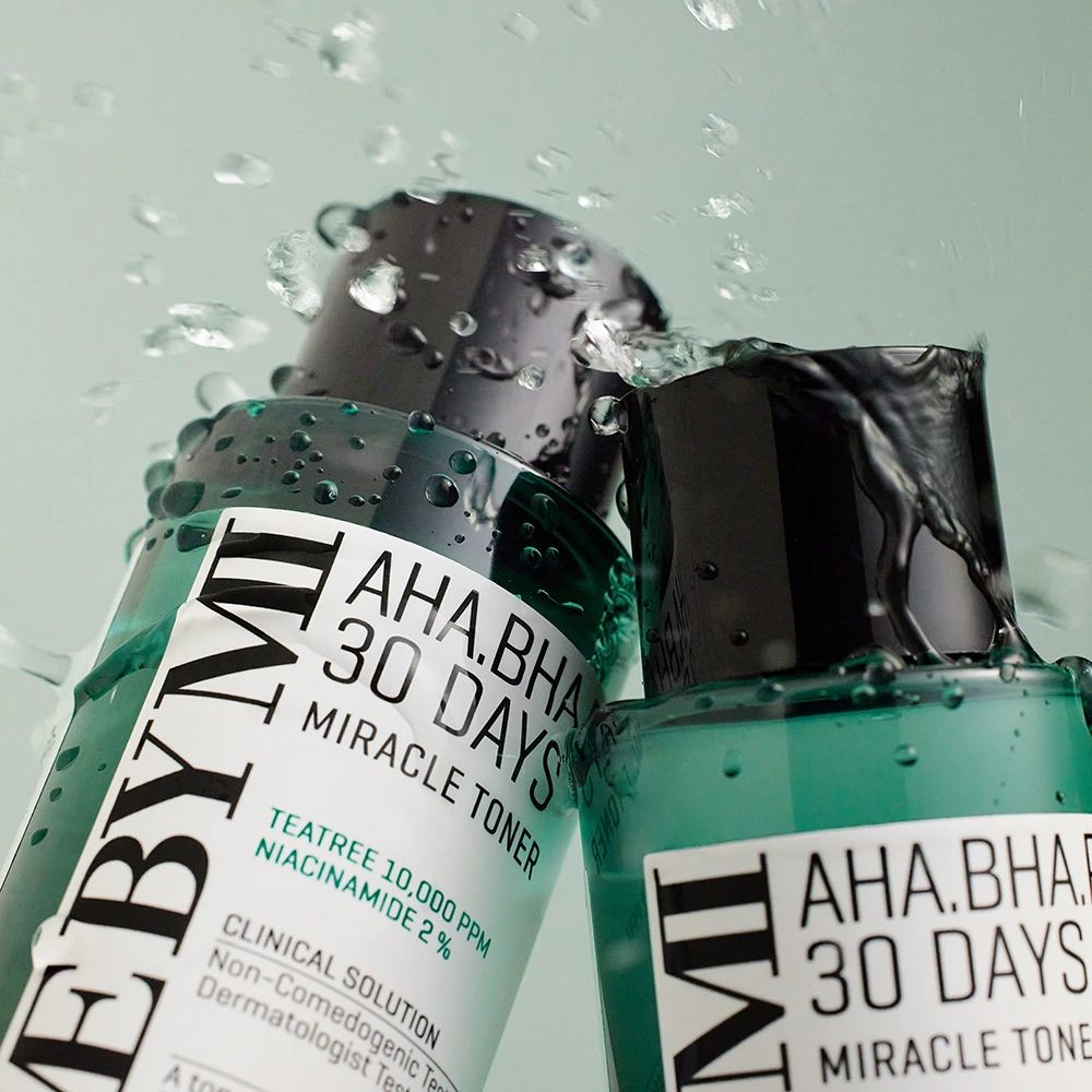 Zwei grüne Flaschen mit schwarzen Deckeln. Aufschrift: AHA.BHA.PHA 30 Days Miracle Toner. Wasser spritzt auf die Flaschen.