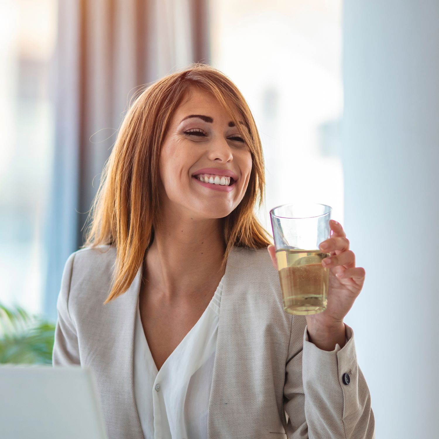 Frau hält Glas mit Flüssigkeit. Sie lächelt. Helle Umgebung.