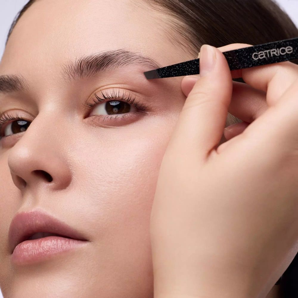 Nahaufnahme einer Person, die mit einer Pinzette Augenbrauen zupft. Aufschrift: Catrice.