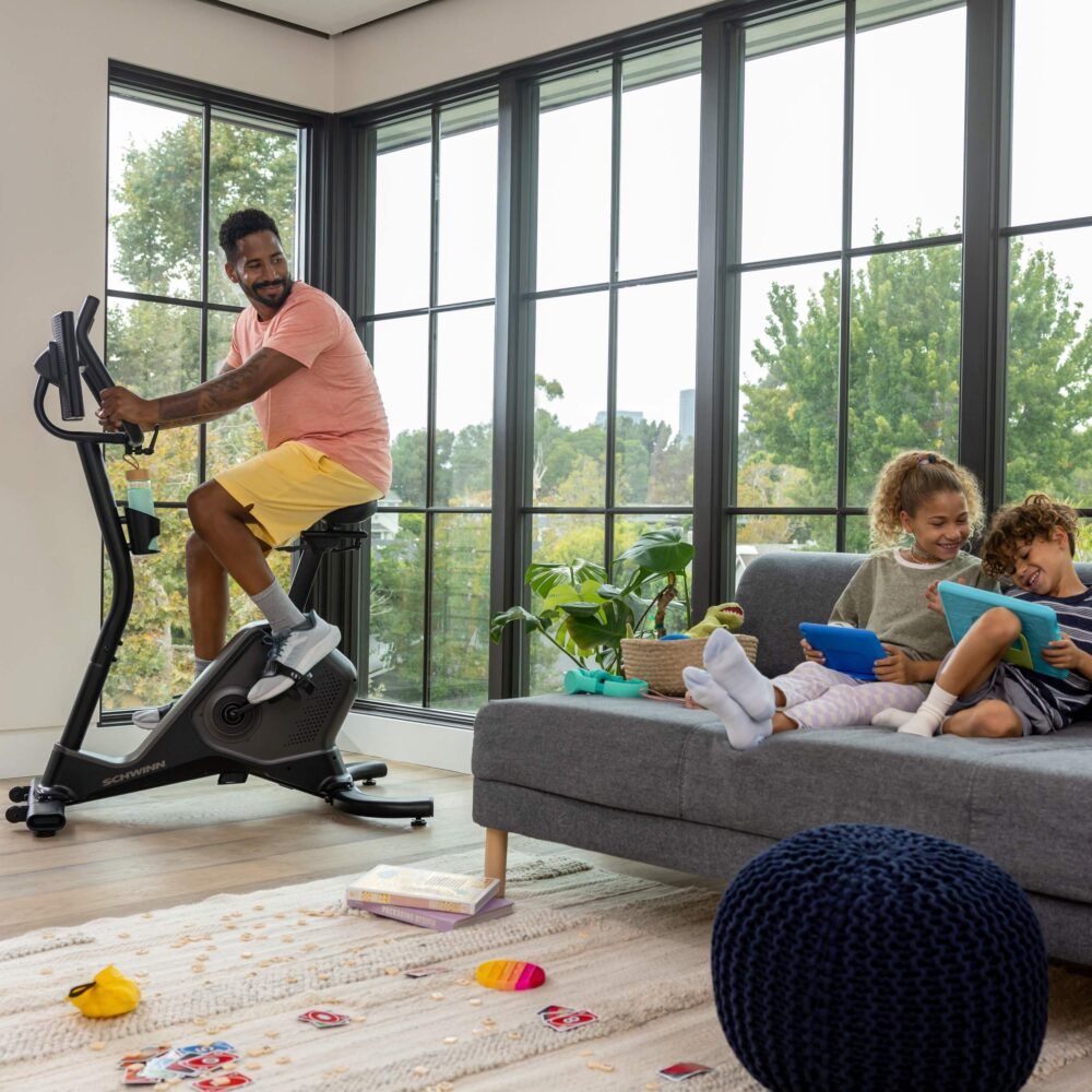 Mann trainiert auf einem Hometrainer. Kinder spielen. Schwinn Fitness 590U.