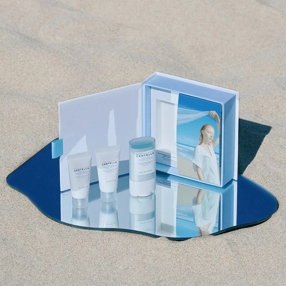 Produkt-Set auf Spiegel. Enthält Sonnenschutzstift und Seren. Spiegelung des Sets und einer Frau am Strand.