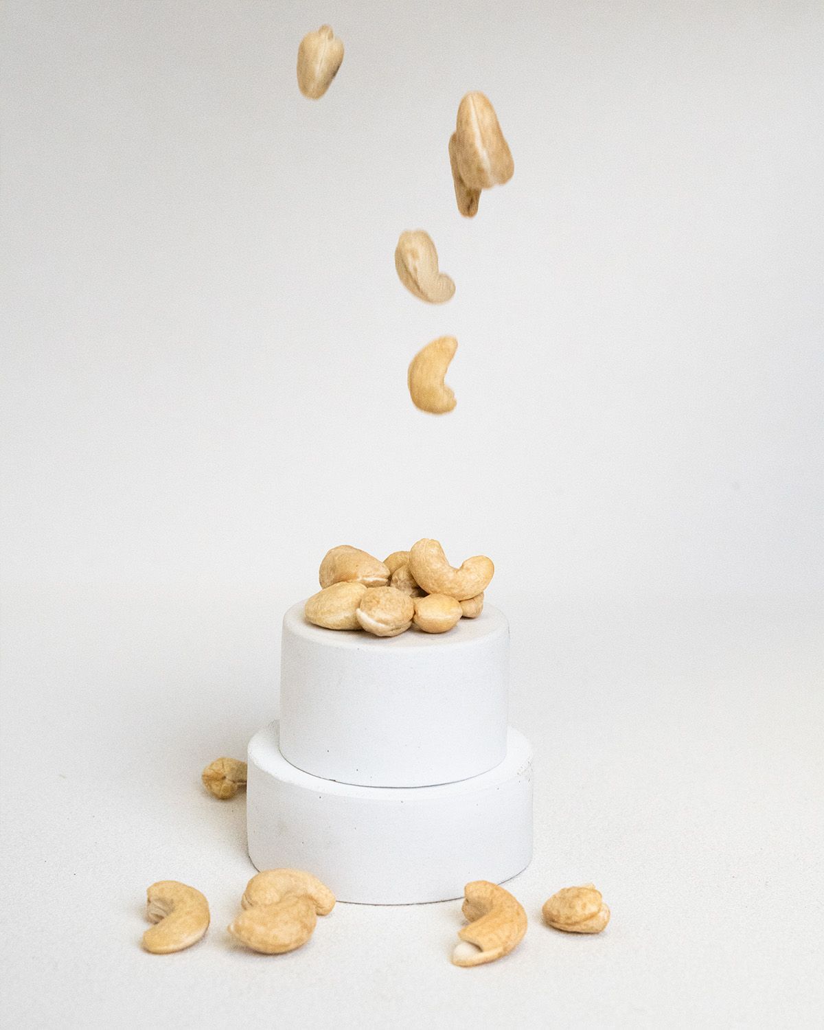 Cashewkerne auf einem weißen Podest. Einige Kerne fallen herunter und liegen daneben.