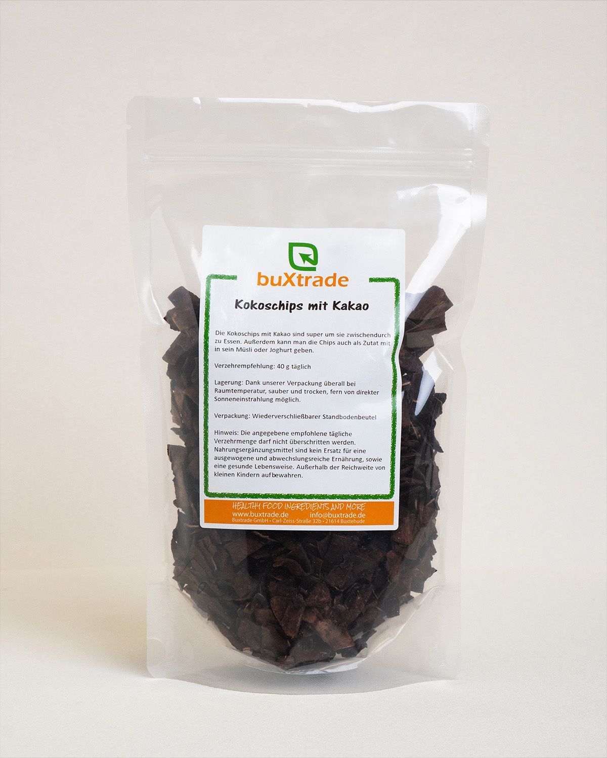 Klare Tüte mit buXtrade Kokoschips mit Kakao. Produktinformationen auf dem Etikett. Weißer Hintergrund.