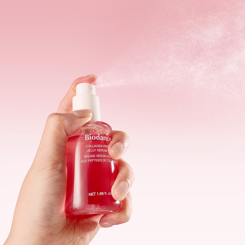 Hand hält eine Sprühflasche mit rotem Serum. Der Sprühkopf zerstäubt feine Tröpfchen.