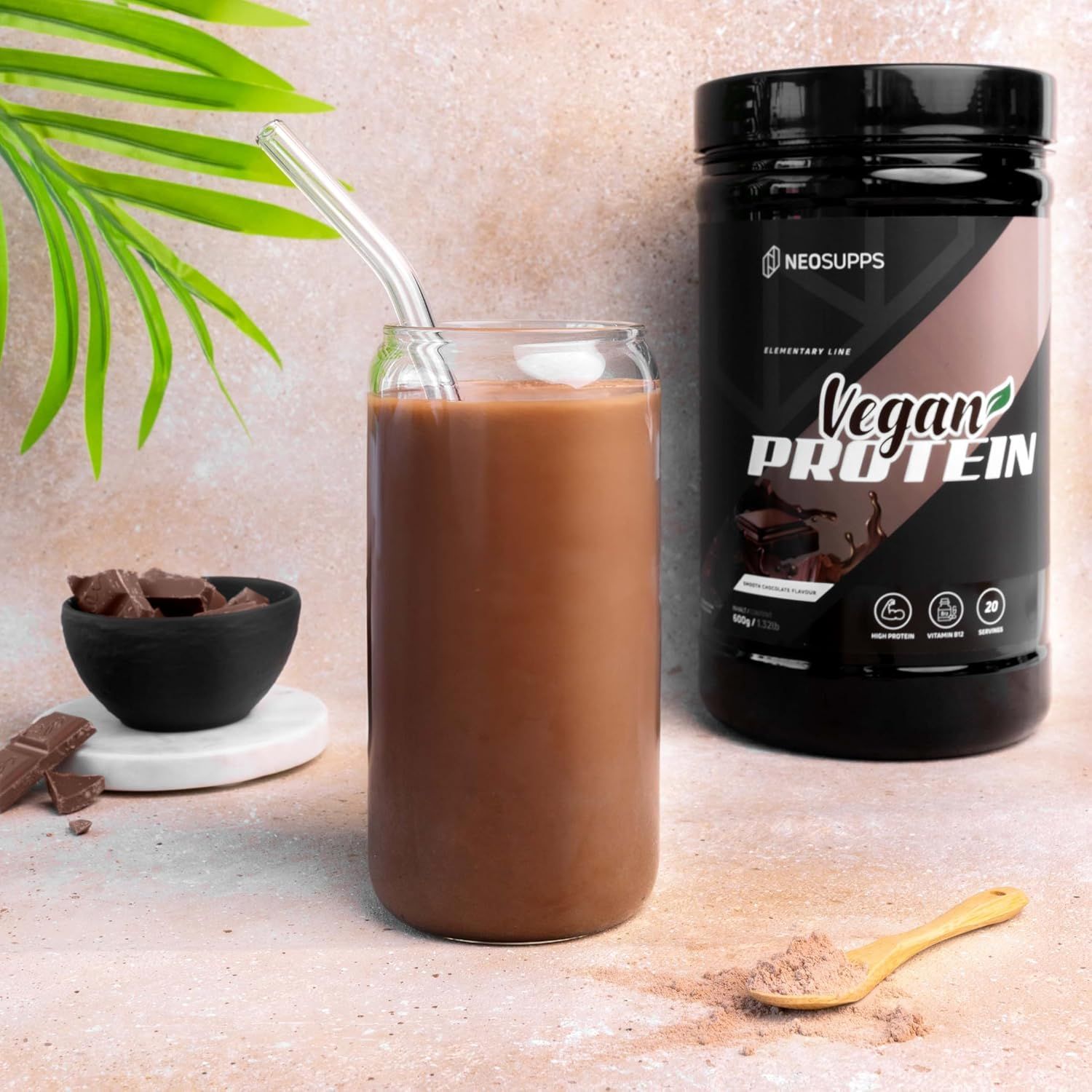 Glas mit Schoko-Drink, daneben Dose Vegan Protein. Aufschrift: Neosupps Vegan Protein. Löffel mit Pulver, Schokoladenstücke.