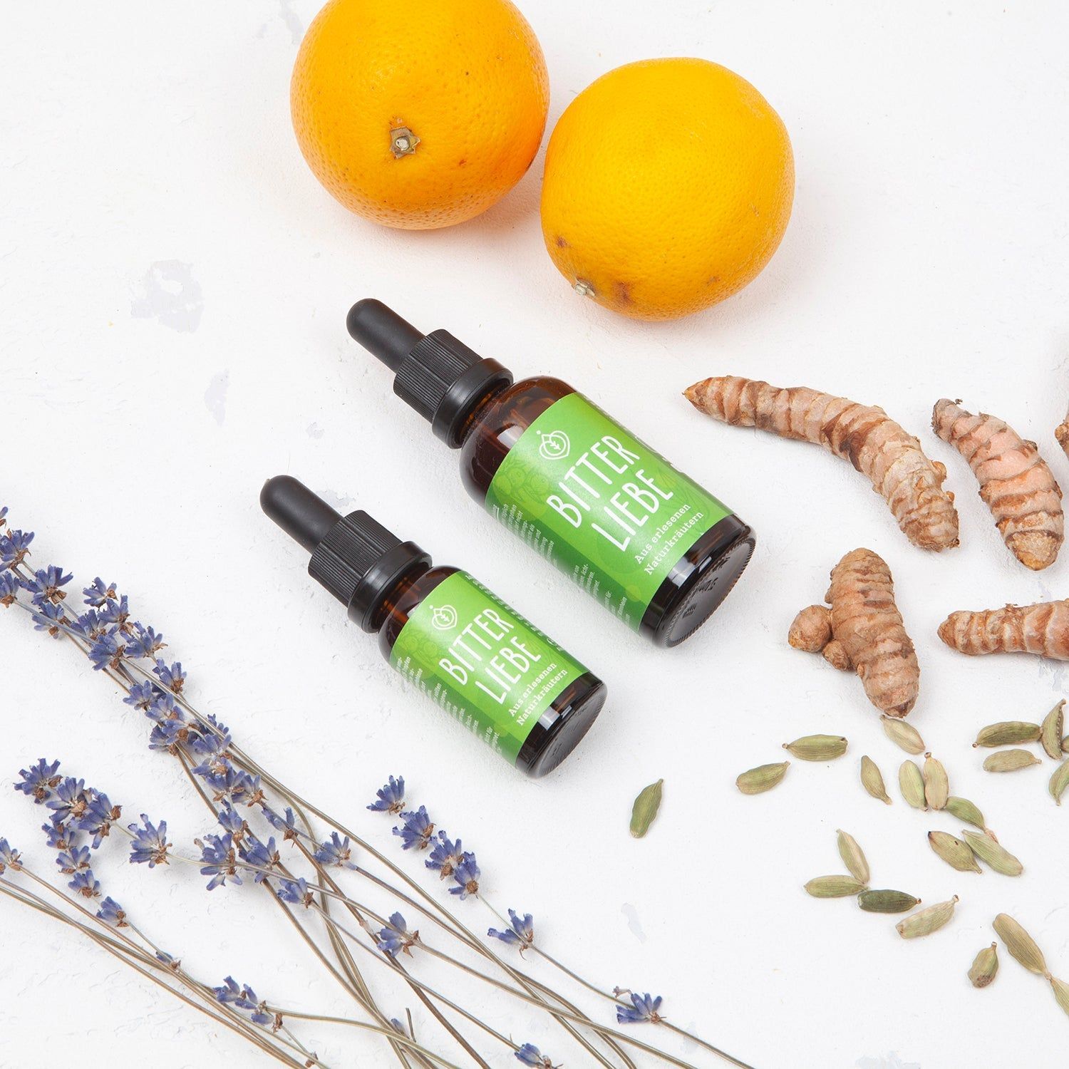 Zwei Flaschen BitterLiebe-Tropfen, daneben Lavendel, Kurkuma und Kardamom.