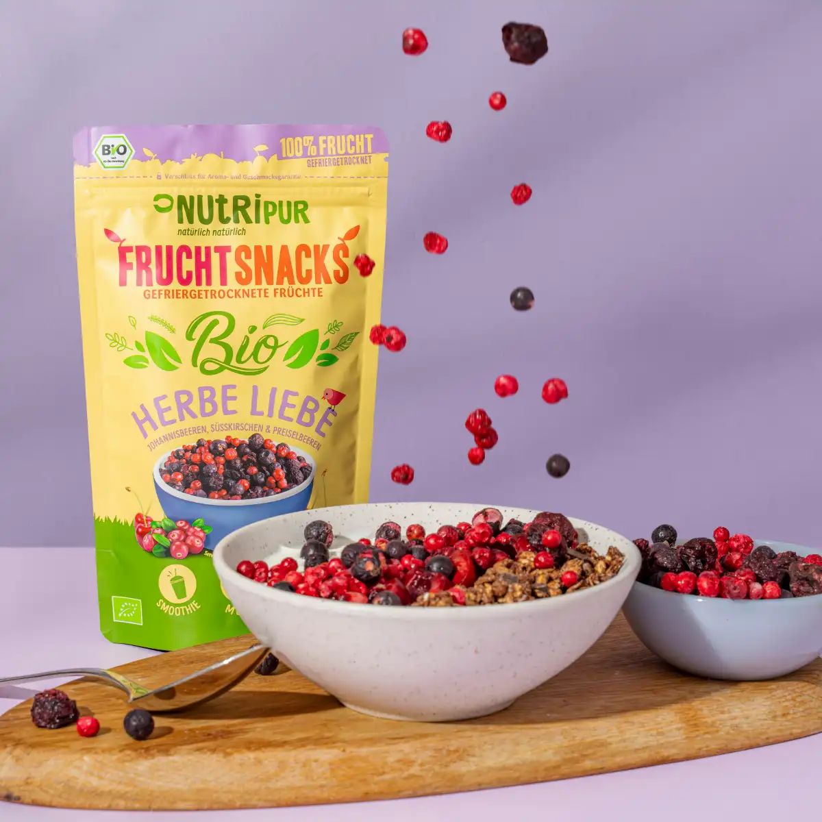 Beutel mit gefriergetrockneten Früchten, Früchte fliegen in Schalen. Aufschrift: Bio, Herbe Liebe, 25g.