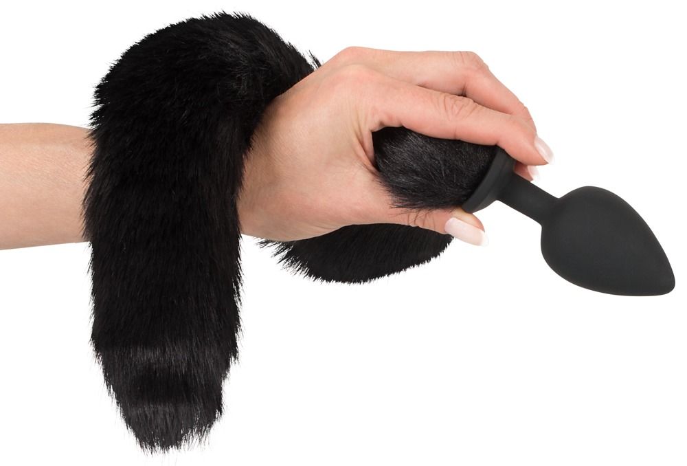 Hand hält schwarzen, pelzigen Schwanz mit schwarzem Plug. Auf weißem Hintergrund.
