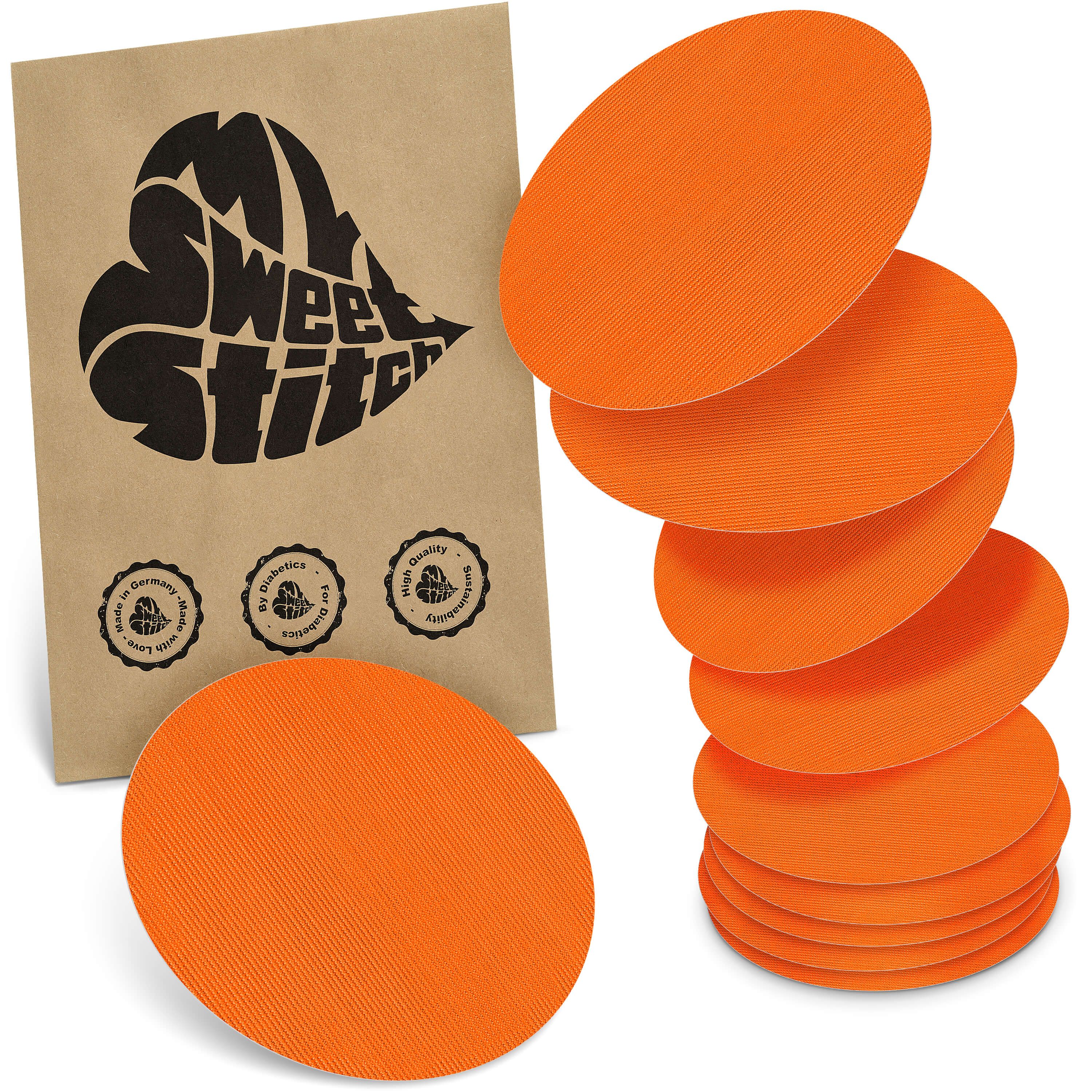 Orange runde Pflaster, gestapelt und einzeln, neben einer braunen Verpackung mit schwarzem Herz-Logo und Qualitätssiegeln.