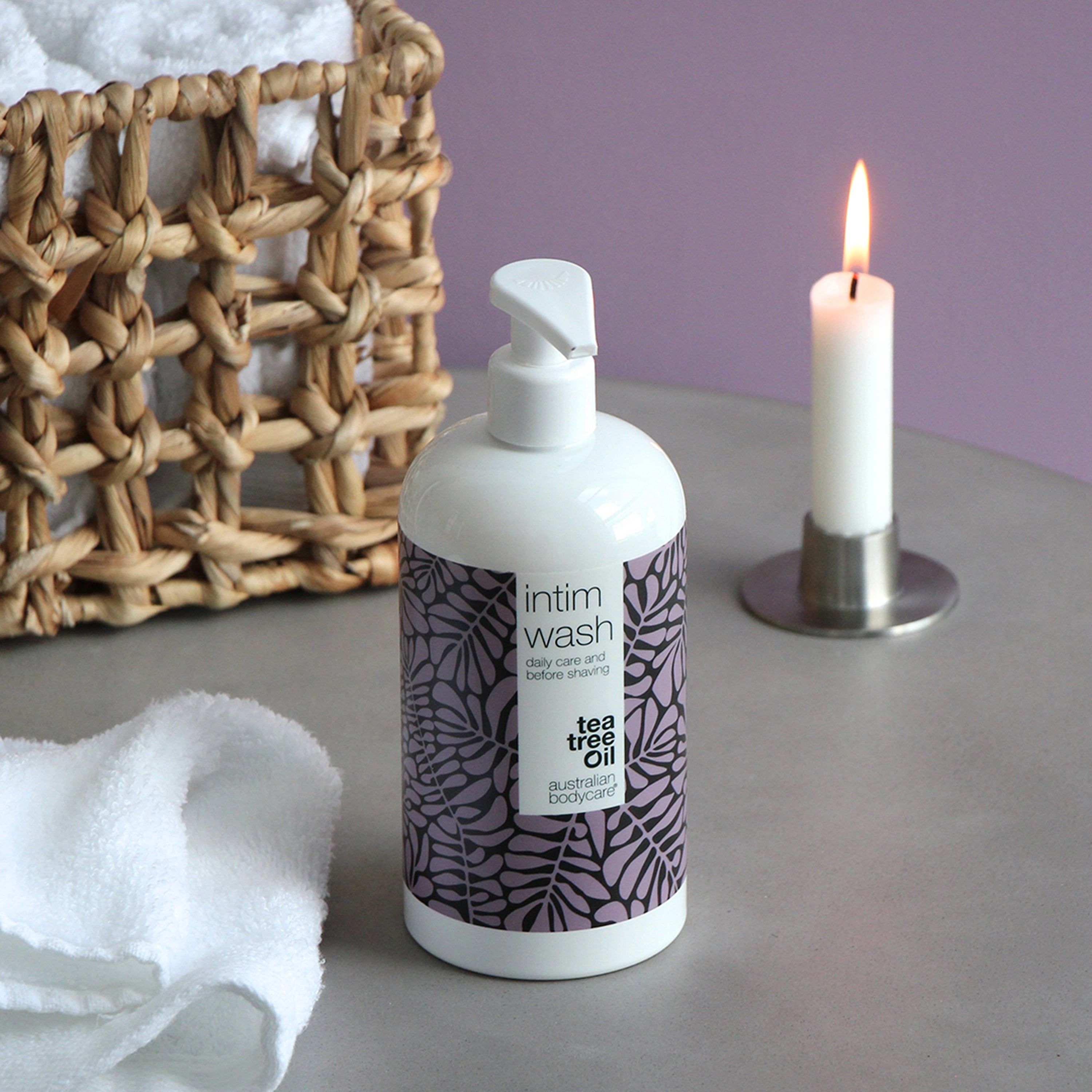 Weißer Spender mit Intimwaschmittel. Lila Blättermuster. Aufschrift: Intim Wash, daily care & before shaving, Australian Bodycare. Kerze.