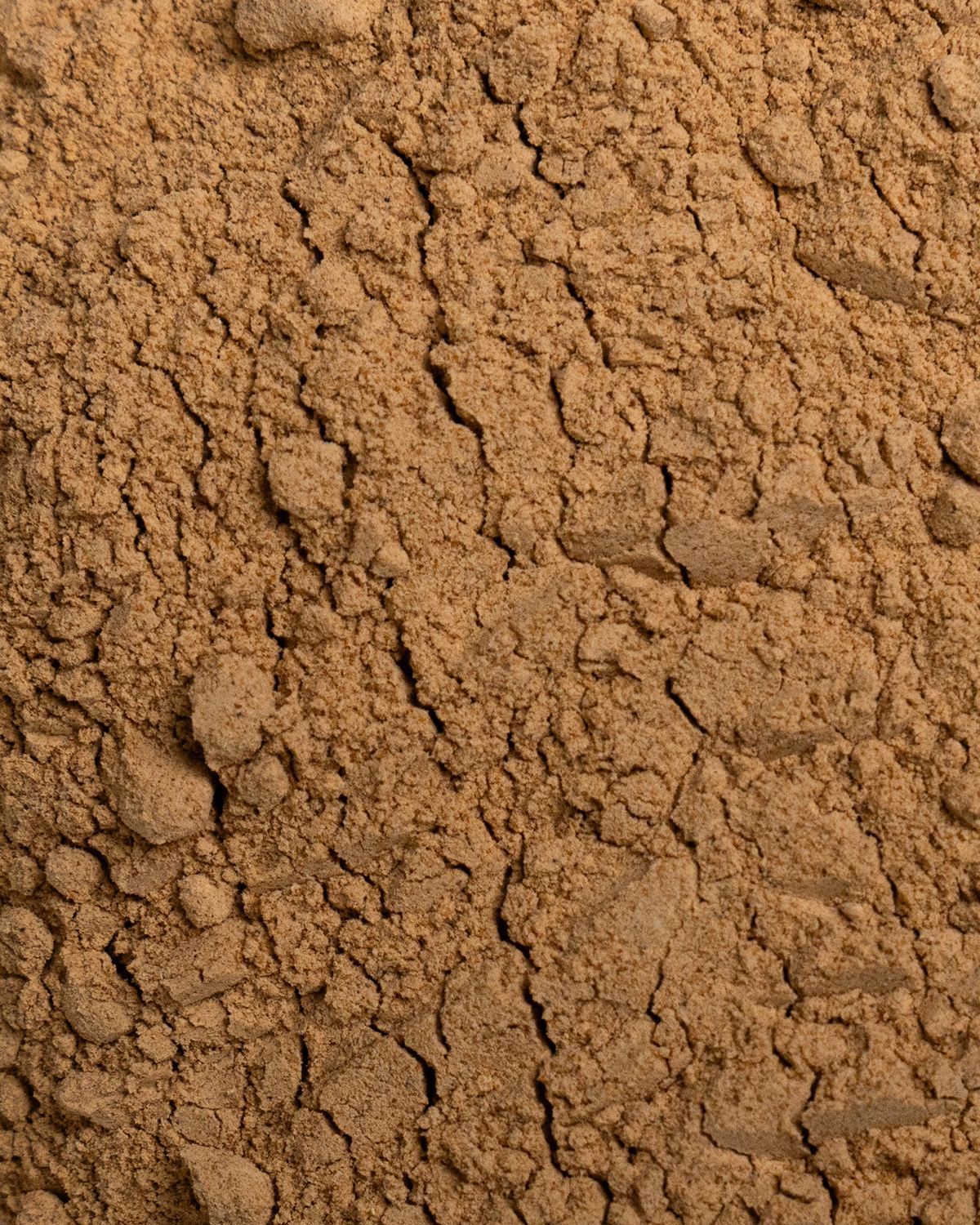 Nahaufnahme von braunem Maca-Pulver. Die Textur ist körnig und leicht rissig.
