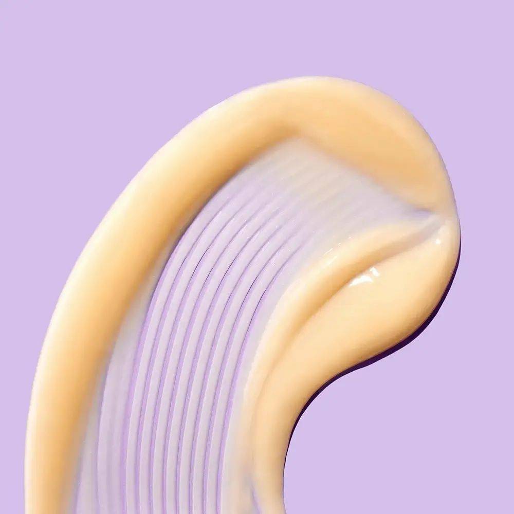 Nahaufnahme eines cremefarbenen Produkts auf lila Hintergrund. Produkt mit geriffelter Textur. Glänzende Oberfläche.