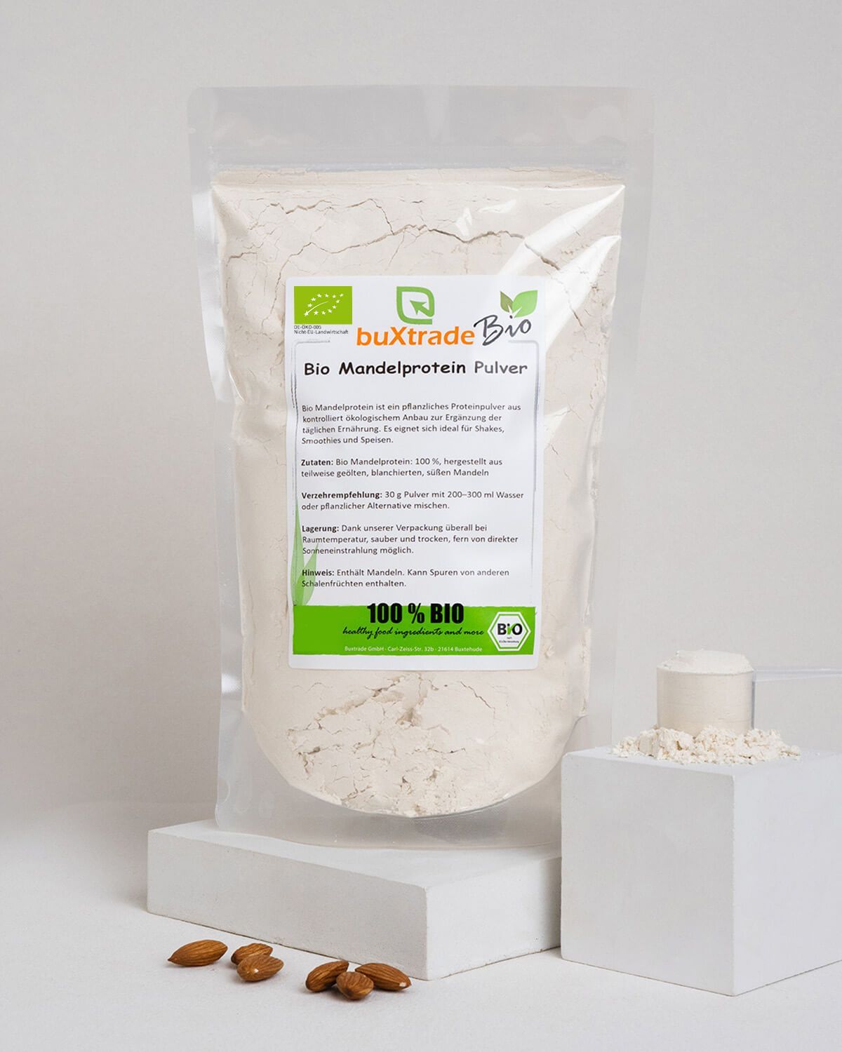 Verpackung und Messlöffel mit buXtrade Bio Mandelprotein Pulver, daneben Mandeln.