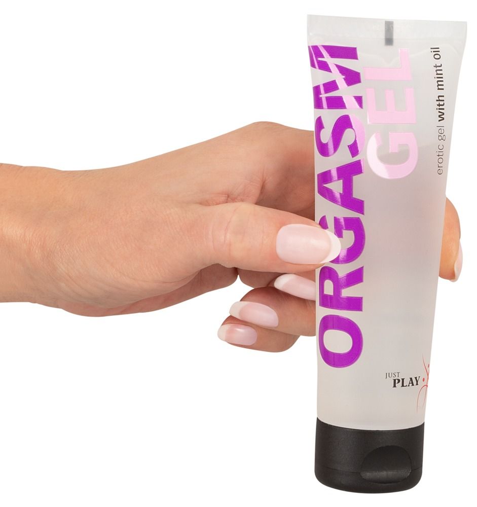 Tube mit Produktnamen, gehalten von einer Hand. Lila Schrift auf weißem Hintergrund. Schwarzer Verschluss.