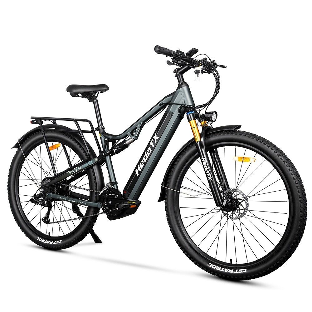 Graues E-Bike HedaTX TX19. Schwarze Reifen, Gepäckträger, Federung. Gelbe Gabel. 27 Gänge. Aufschrift HedaTX.