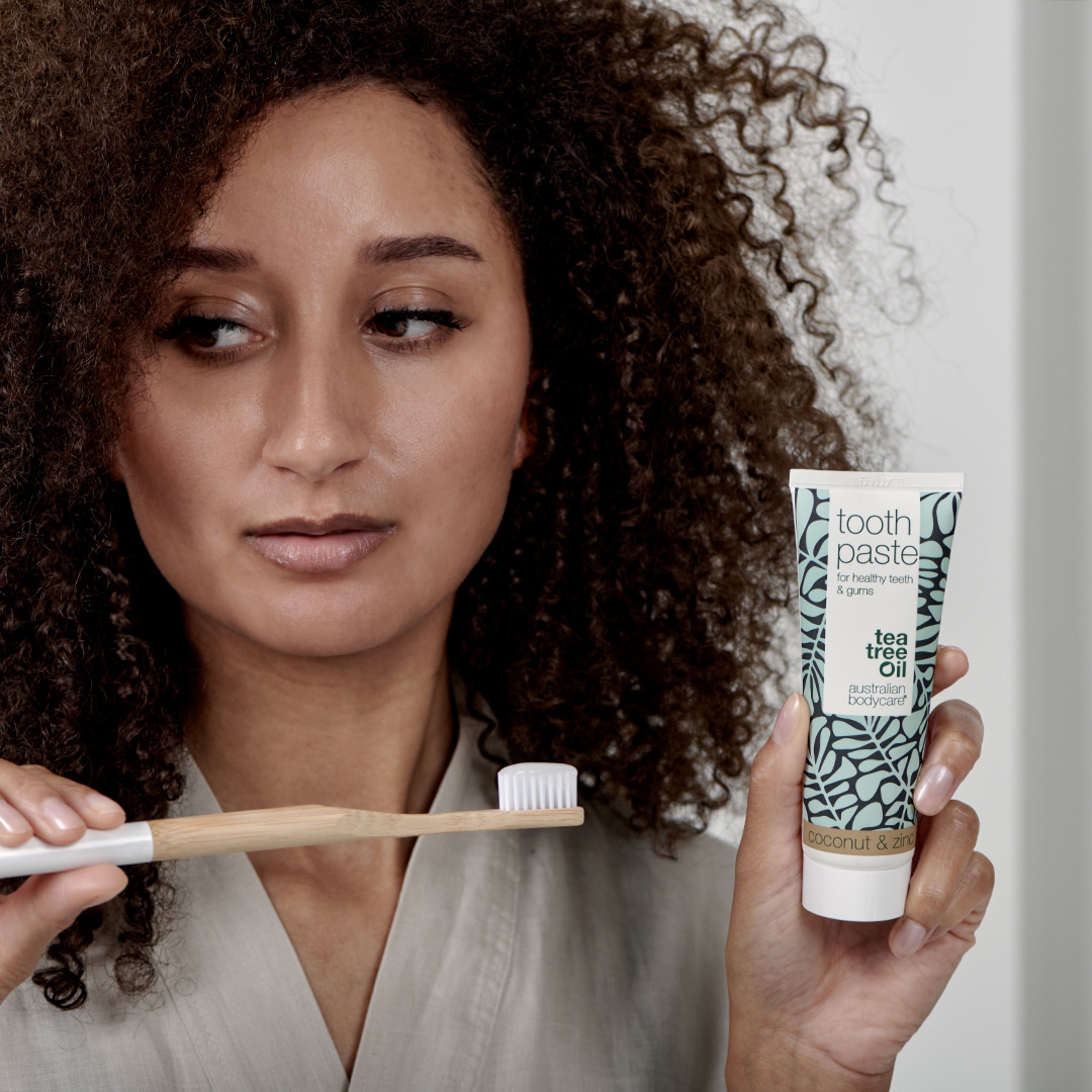 Frau mit Zahnbürste und Zahnpasta-Tube. Aufschrift: Toothpaste, Australian Bodycare, Tea Tree Oil.