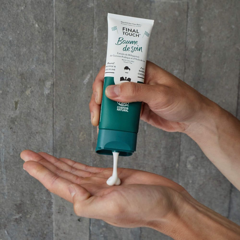 Eine Tube mit weißer Creme, die in eine Hand gedrückt wird. Die Tube ist grün und weiß mit dem Schriftzug "Baume de soin".