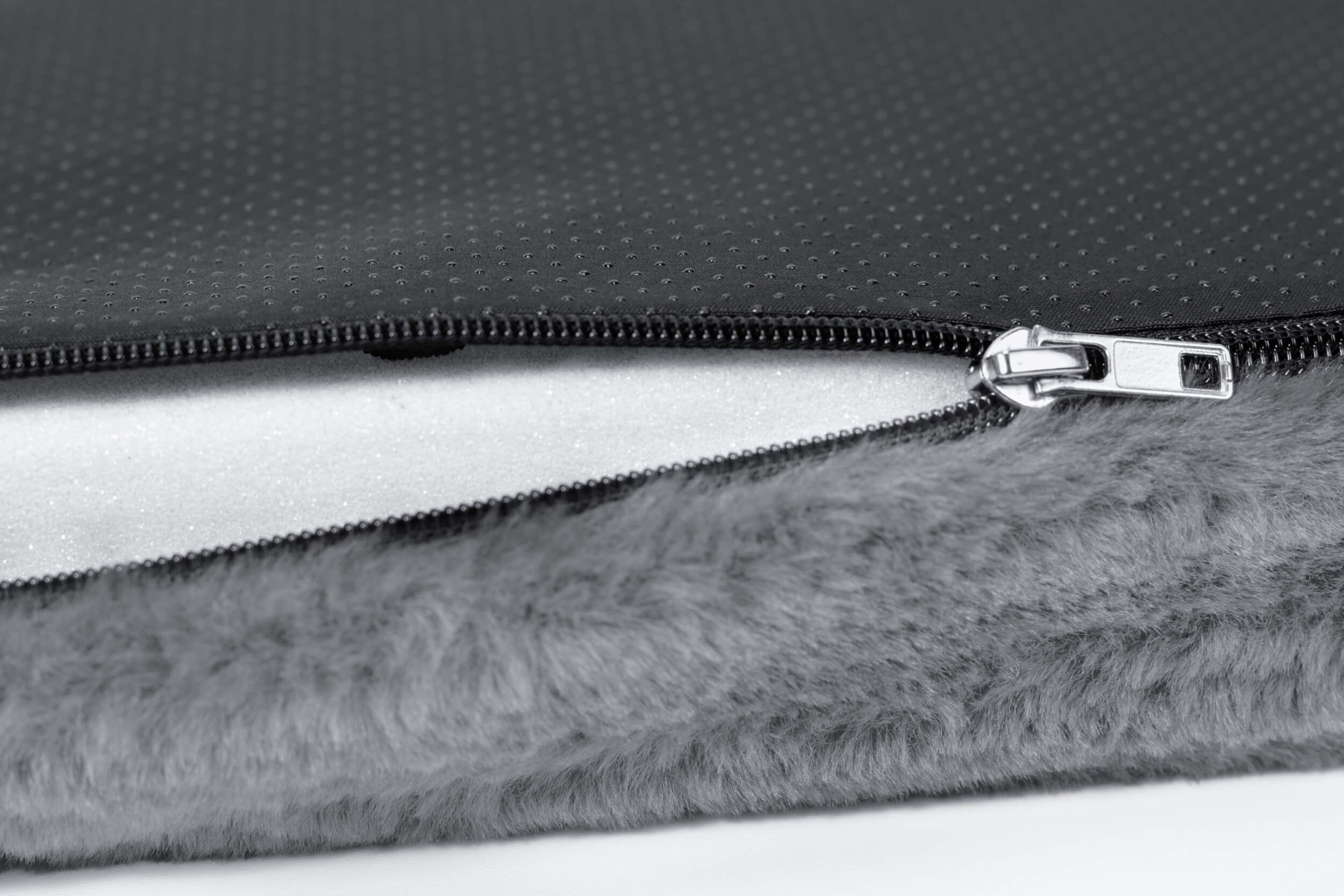 Nahaufnahme einer grauen Hundematratze mit Reißverschluss. Innen Schaumstoff. Fellstruktur.