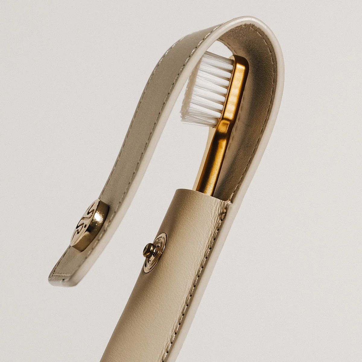 Goldene Zahnbürste in einer hellen Lederhülle. Hülle mit Knopfverschluss.