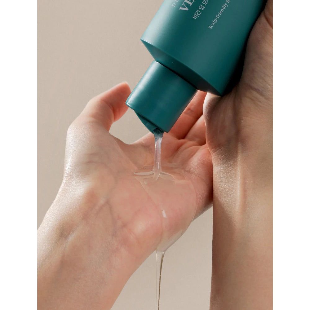 Hände halten eine Flasche, aus der Shampoo fließt. Klare Flüssigkeit. Helle Umgebung.