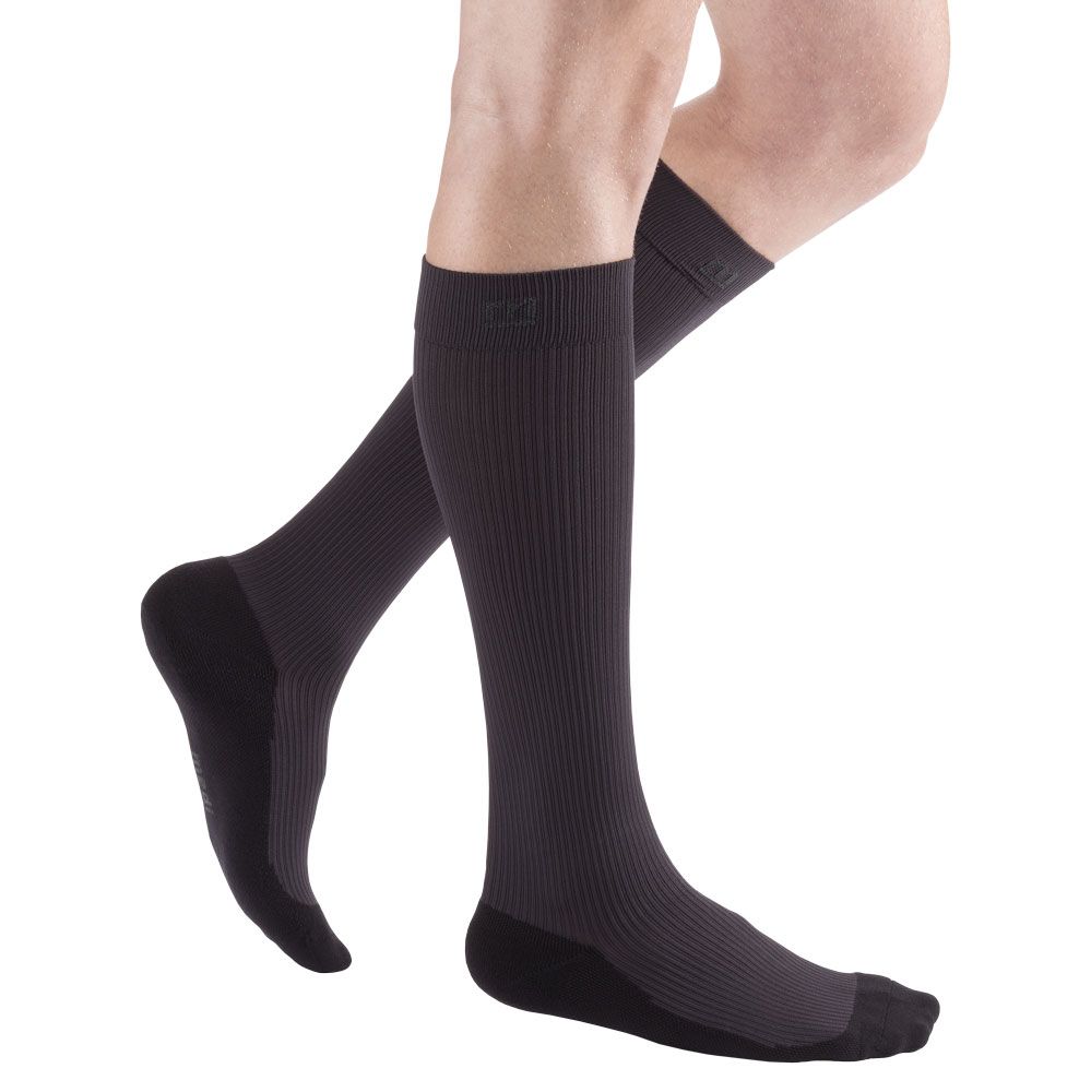 Dunkelgraue Kompressionsstrümpfe am Bein. Rippstrickmuster, schwarze Fußspitze und Ferse. Trikotabschlussrand.