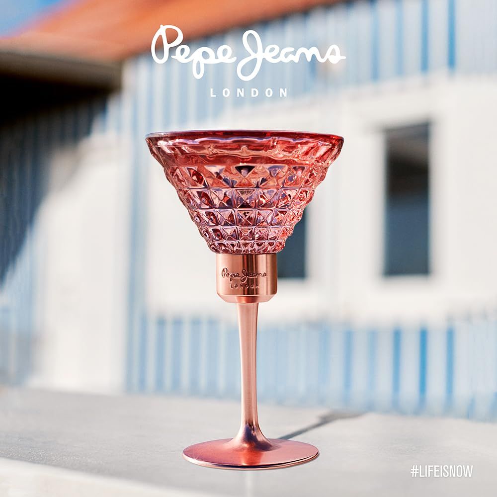Parfümflakon in Cocktailglasform, rosa. Hintergrund: Gebäude mit blau-weißen Streifen. Markenname.