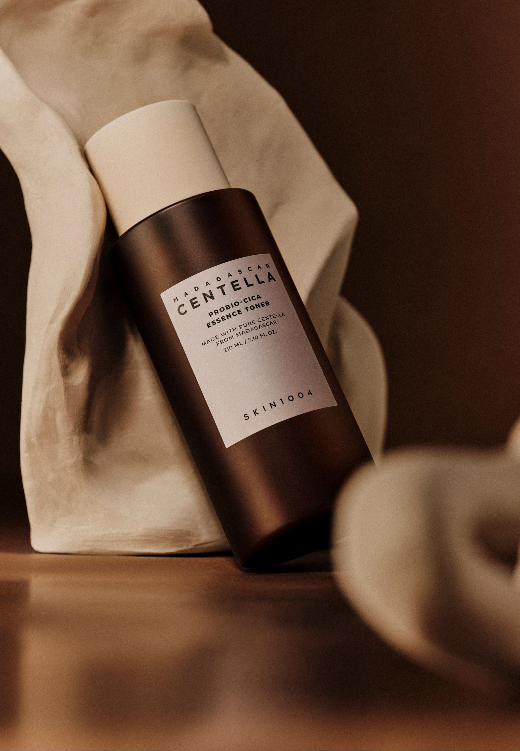Braune Flasche mit weißem Deckel, vor weißem Stoff. Text: MADAGASCAR CENTELLA, PROBIO-CICA Essence Toner, SKIN1004.