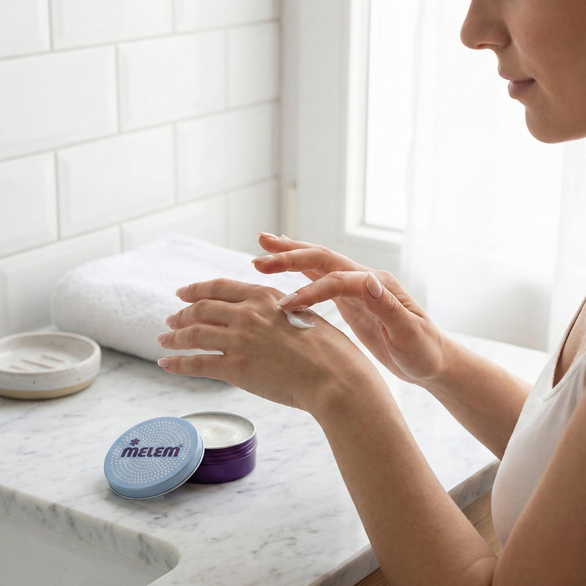 Person trägt Creme auf. Offene, runde Dose mit "MELEM"-Logo. Dose steht neben einer Person, die Creme auf die Hand aufträgt.