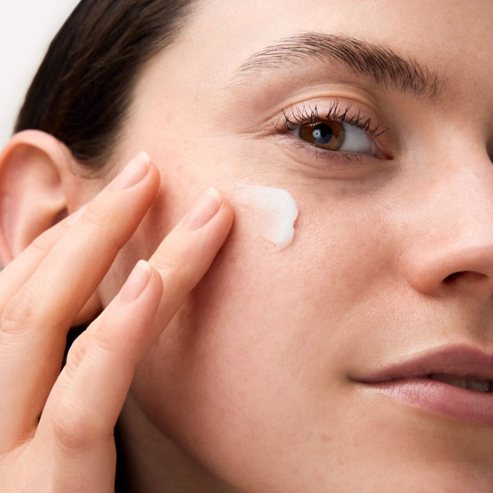 Nahaufnahme einer Frau, die Creme auf ihr Gesicht aufträgt. Helle Haut, Finger berühren die Haut.