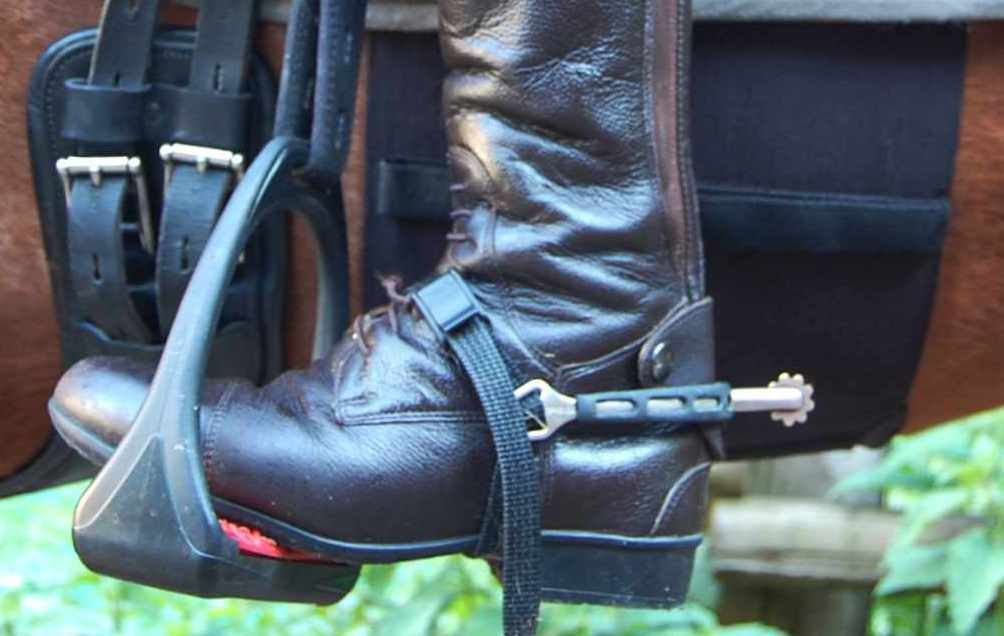 Detailansicht eines Sporenschutzes am Stiefel. Schwarzer Schutz mit silbernem Sporen.