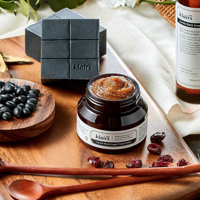 Glas mit Creme, daneben weitere Produkte. Aufschrift: dear, klairs Gentle Black Sugar Facial Polish.