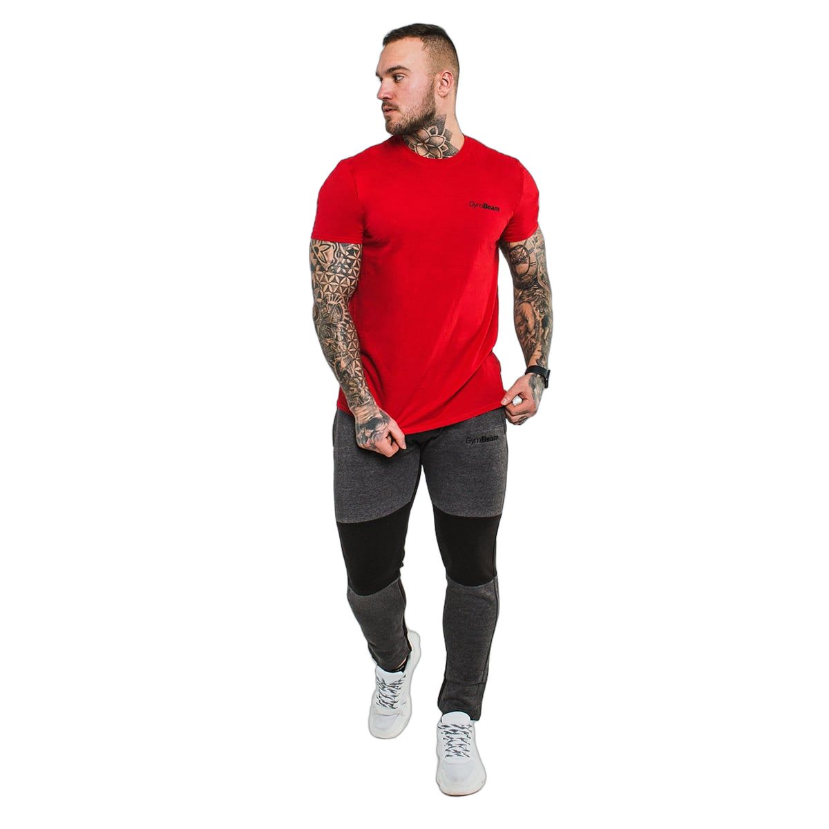 Mann in rotem GymBeam T-Shirt und grauer Hose, steht vor weißem Hintergrund.