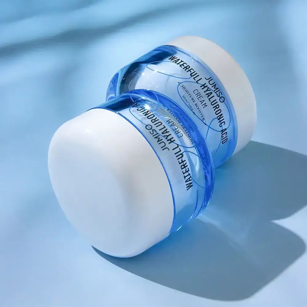 Zwei Tiegel JUMISO Waterfull Hyaluronic Acid Face Cream. Blaue Verpackung mit weißem Deckel. Auf einer blauen Oberfläche.