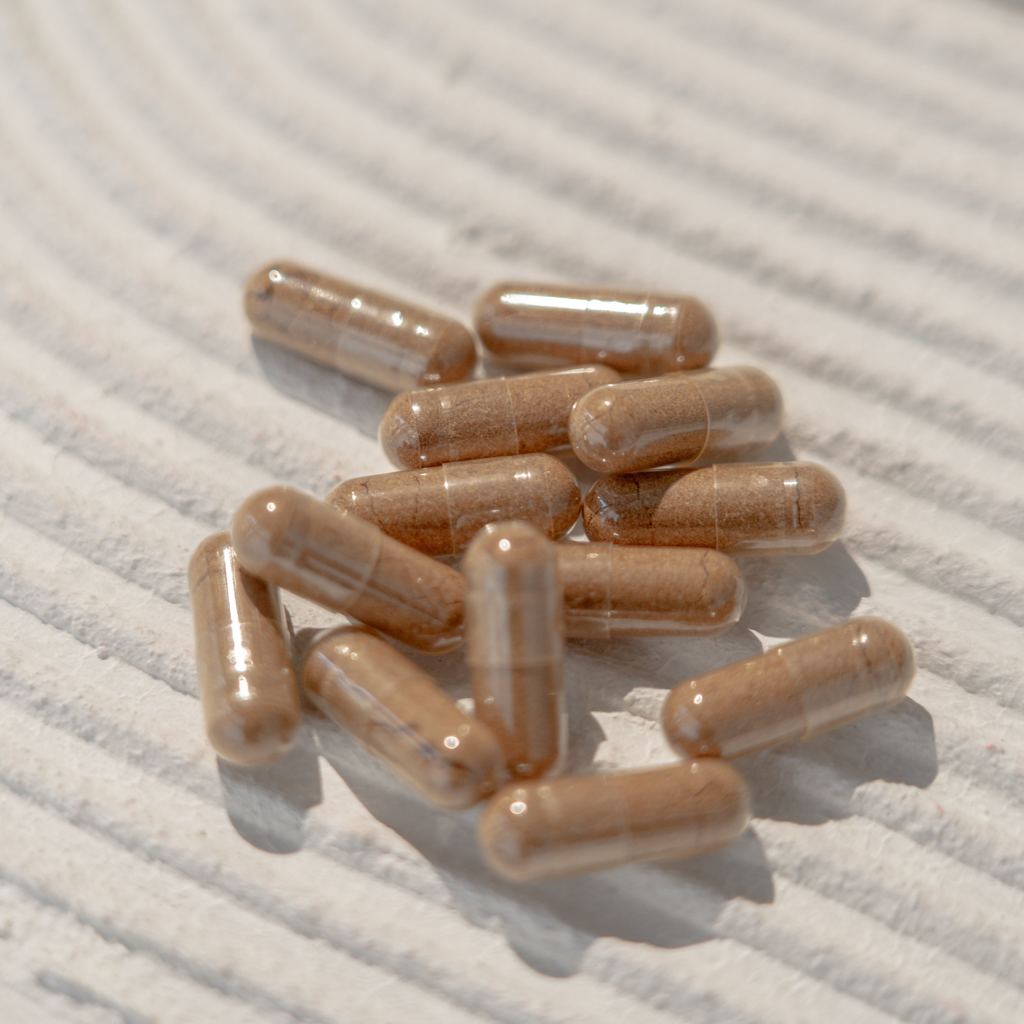 Ein Haufen brauner Rhodiola Rosea Kapseln auf einer strukturierten Oberfläche.