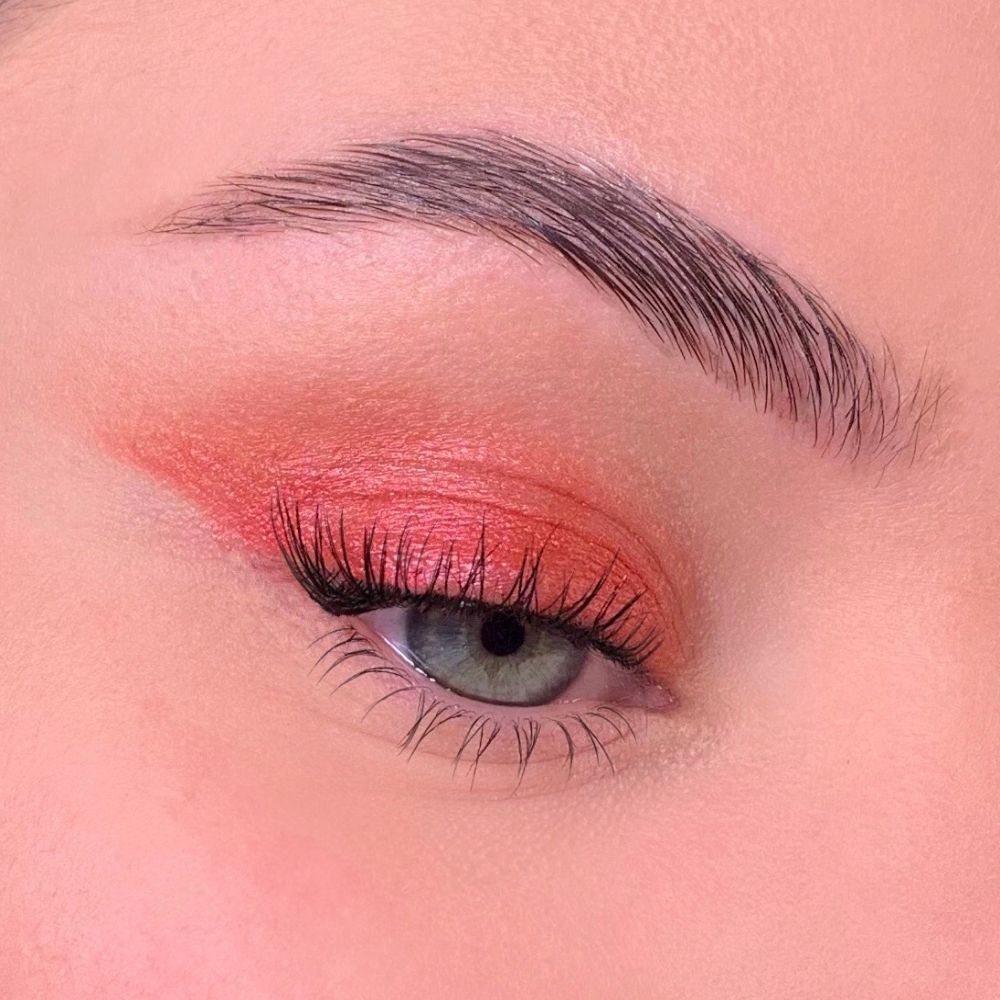 Auge mit rotem Lidschatten. Oberes Augenlid mit rotem Lidschatten bedeckt. Wimpern und Augenbraue sichtbar.