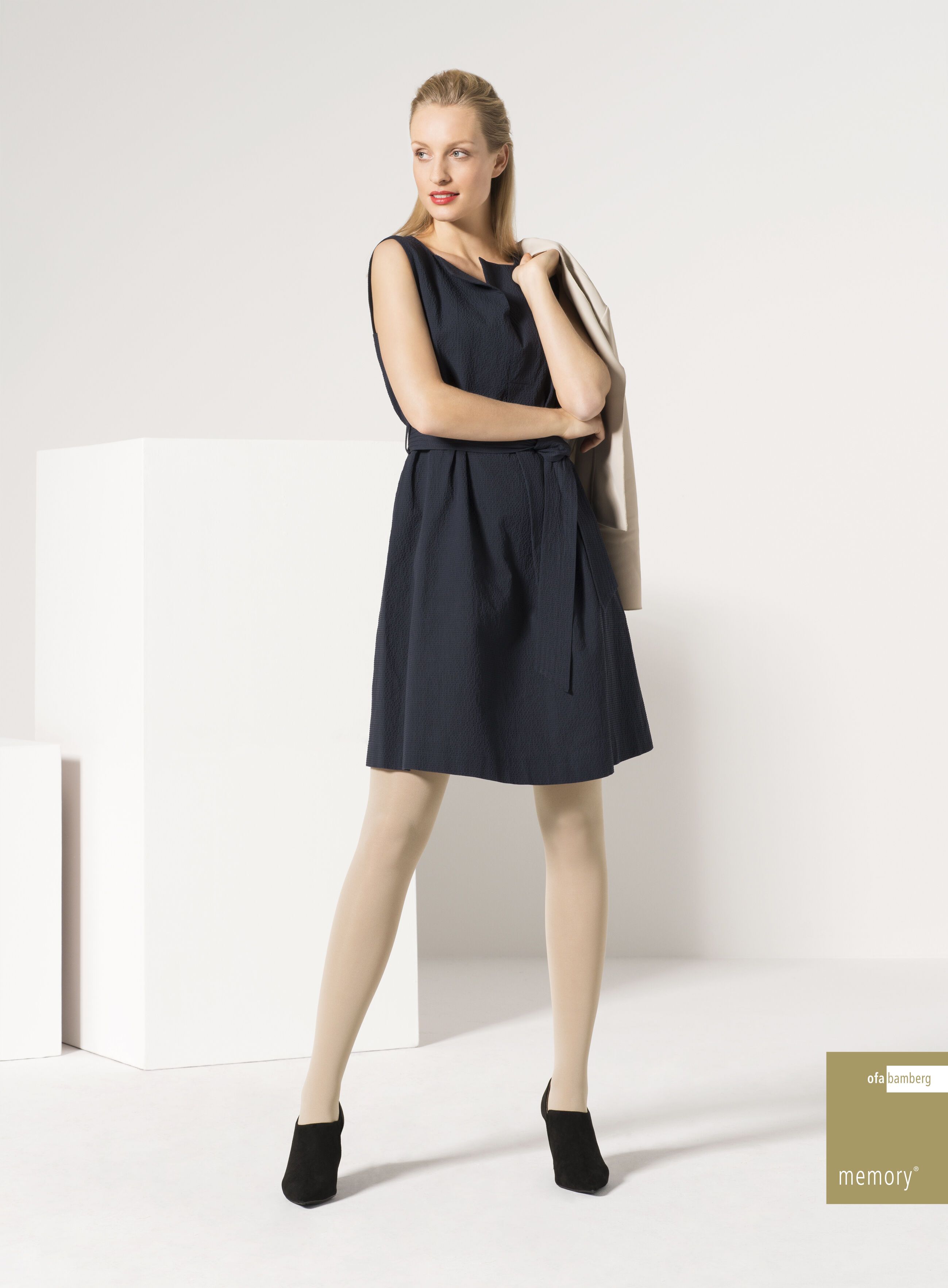 Dunkelblaues Umstandskleid mit Gürtel. Frau trägt Strumpfhose und Schuhe. Beige Jacke über der Schulter. Logo: OFA Bamberg Memory.