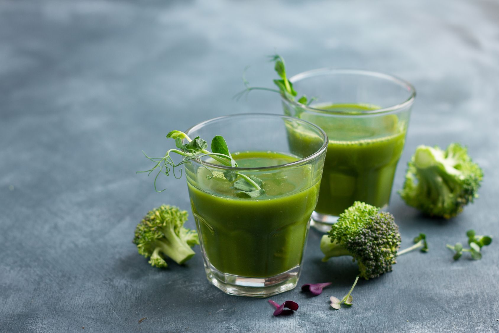 Zwei Gläser grüner Smoothie mit Brokkoli und Sprossen. Auf grauem Untergrund.