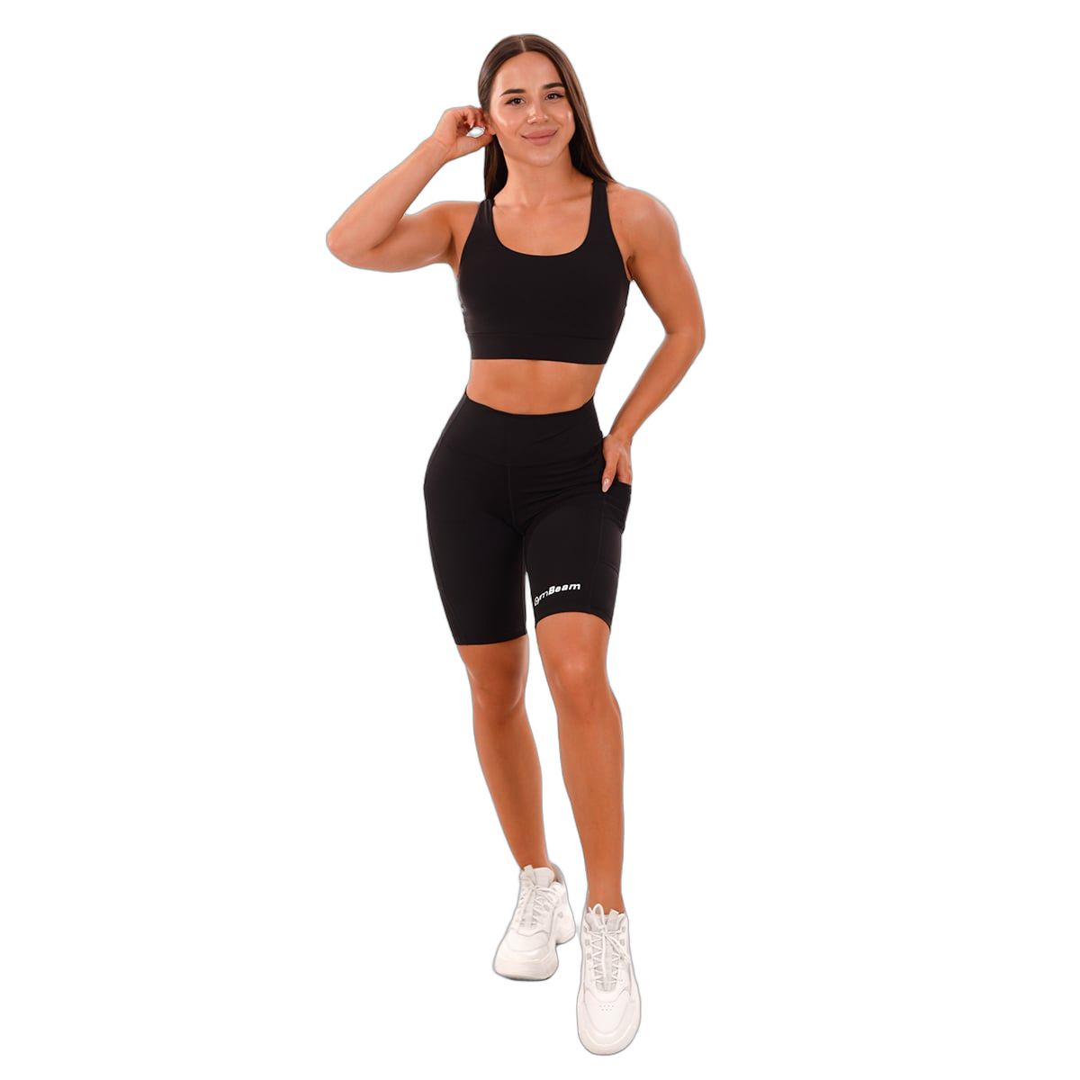 Frau in schwarzen Biker-Shorts mit hoher Taille, Sport-BH und weißen Sneakern.