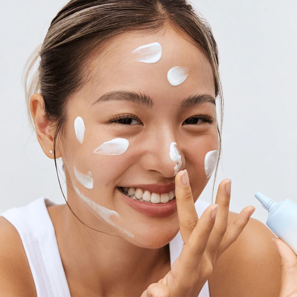 Frau trägt weiße Sonnencreme auf ihr Gesicht auf, hält eine Tube.