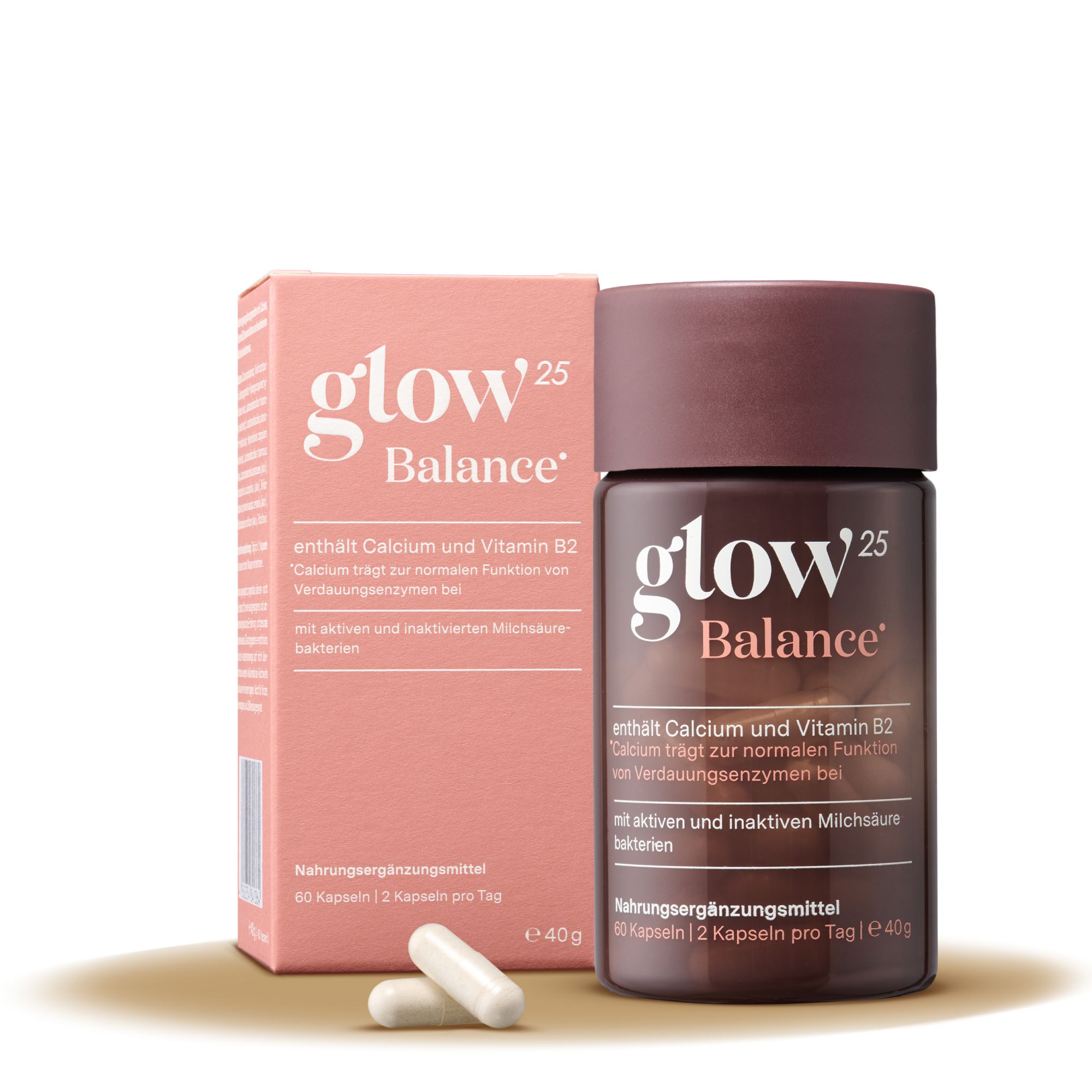 Rosa Schachtel und braune Dose mit Kapseln. Aufschrift: Glow25 Balance. Enthält Calcium und Vitamin B2. Nahrungsergänzungsmittel. Zwei Kapseln liegen daneben.