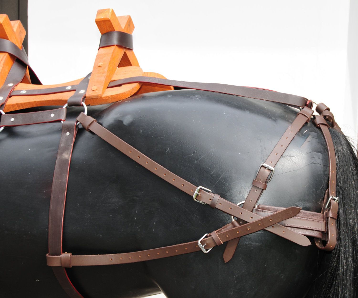 Holz-Packsattel mit Lederbegurtung. Braune Lederriemen, Holzkonstruktion. Rückansicht auf schwarzem Pferd.