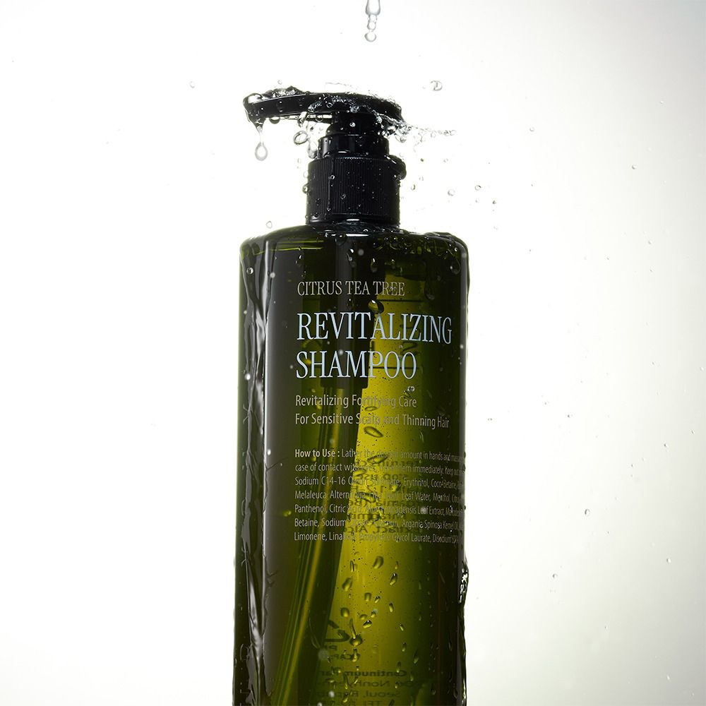 Grüne Shampoo-Flasche mit schwarzem Pumpverschluss. Wasser spritzt auf die Flasche. Aufschrift: Revitalizing Shampoo.