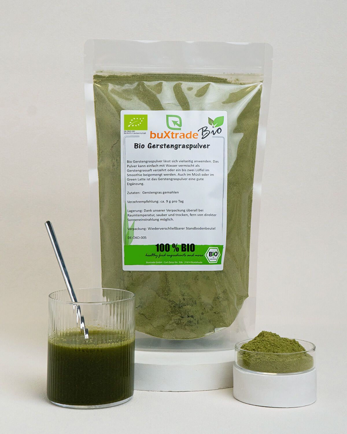 Verpackung von Bio Gerstengraspulver neben einem Glas mit Getränk und einer Schale Pulver.