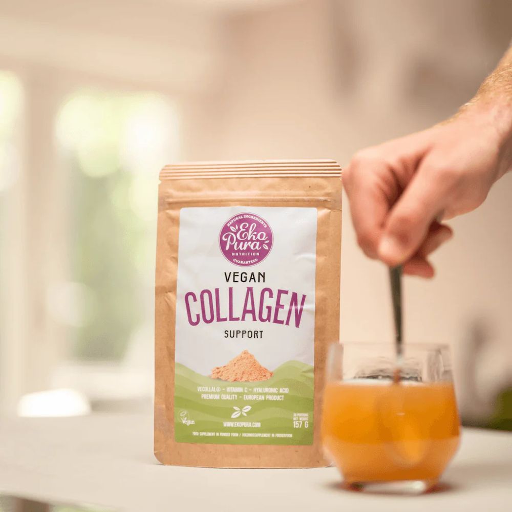 Beutel mit Aufschrift Vegan Collagen Support. Löffel rührt in Glas. Hand hält Löffel. Hintergrund: Küche.
