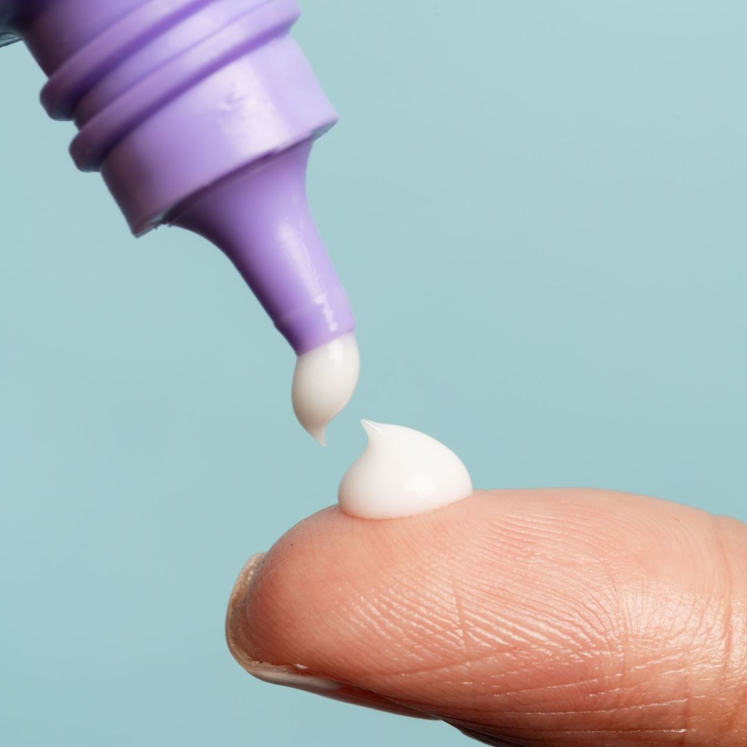 Creme wird aus einer lila Tube auf einen Finger gedrückt. Der Creme-Tropfen ist weiß.