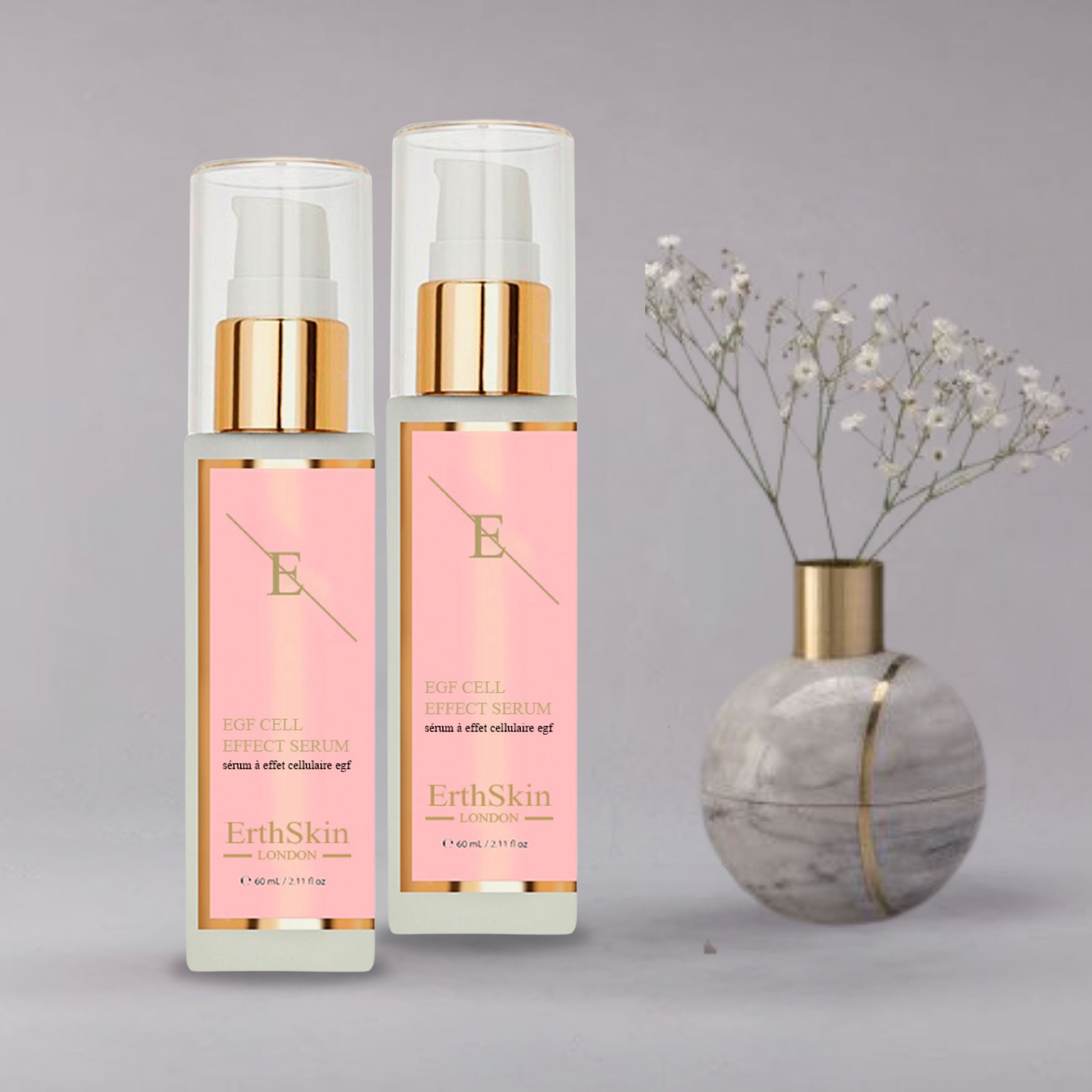 Zwei Flaschen ErthSkin London EGF ZELL EFFEKTSERUM. Rosa Etiketten mit Text und Logo. Goldfarbene Pumpköpfe und transparente Kappen. Neben Vase mit Blumen.