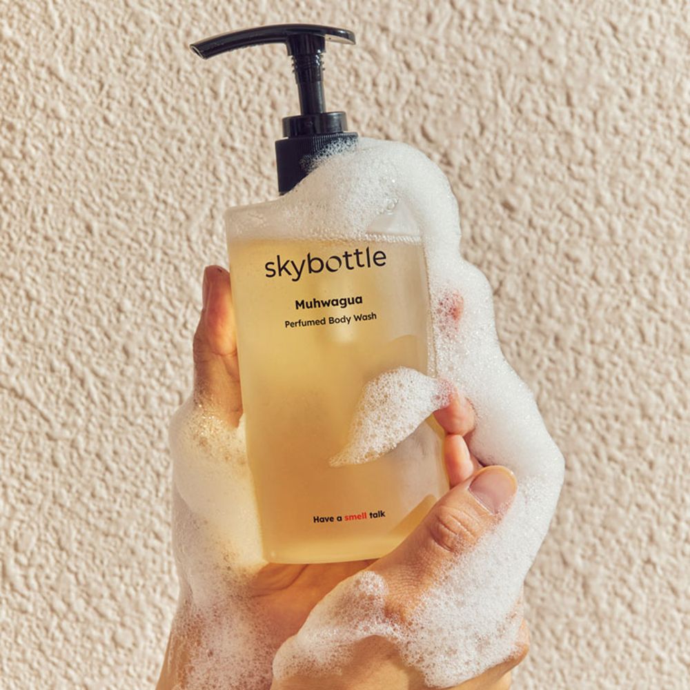 Eine Person hält eine Flasche SKYBOTTLE Muhwagua Duschgel, umgeben von Schaum. Aufschrift: Muhwagua, Perfumed Body Wash. Slogan: Have a smell talk.